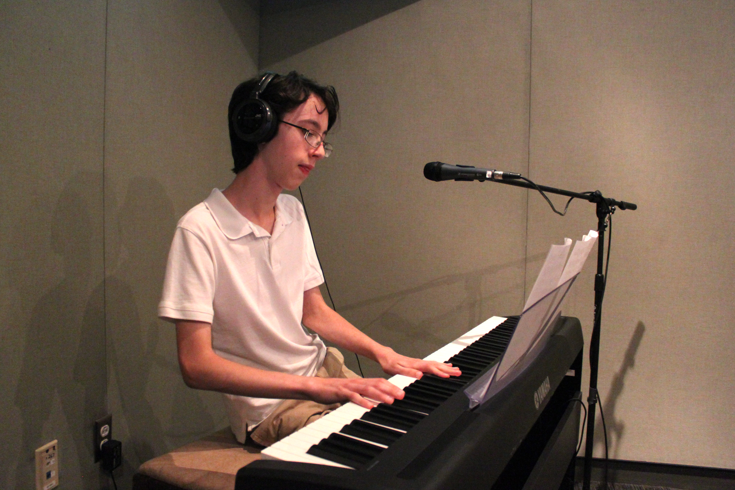 A teen wearing headphones playing a piano keyboard sitting behind a microphone in a radio studio