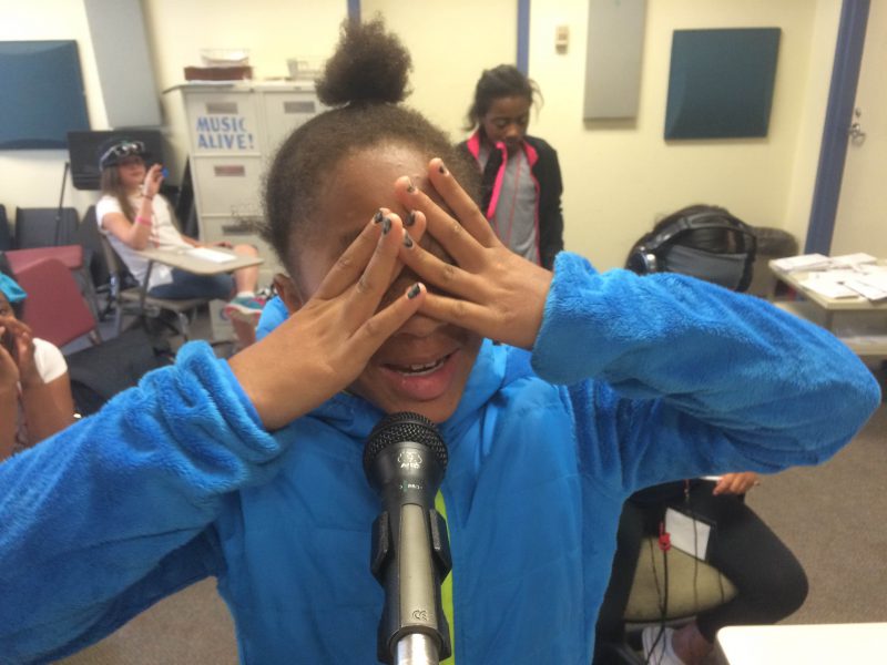 A youth standing behind a microphone covering their face with their hands