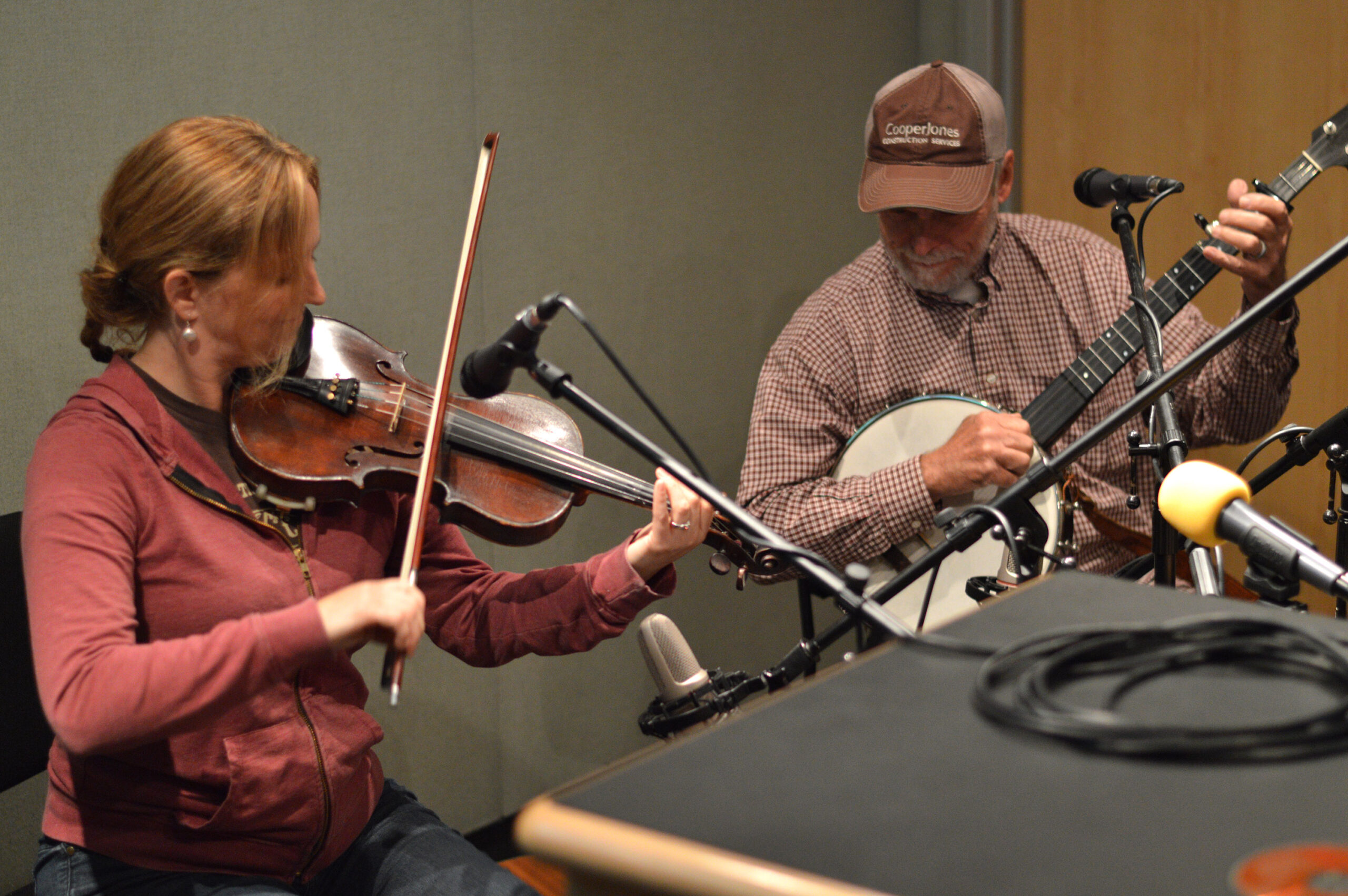 An adult playing a violin and an adult playing a banjo in a radio studio