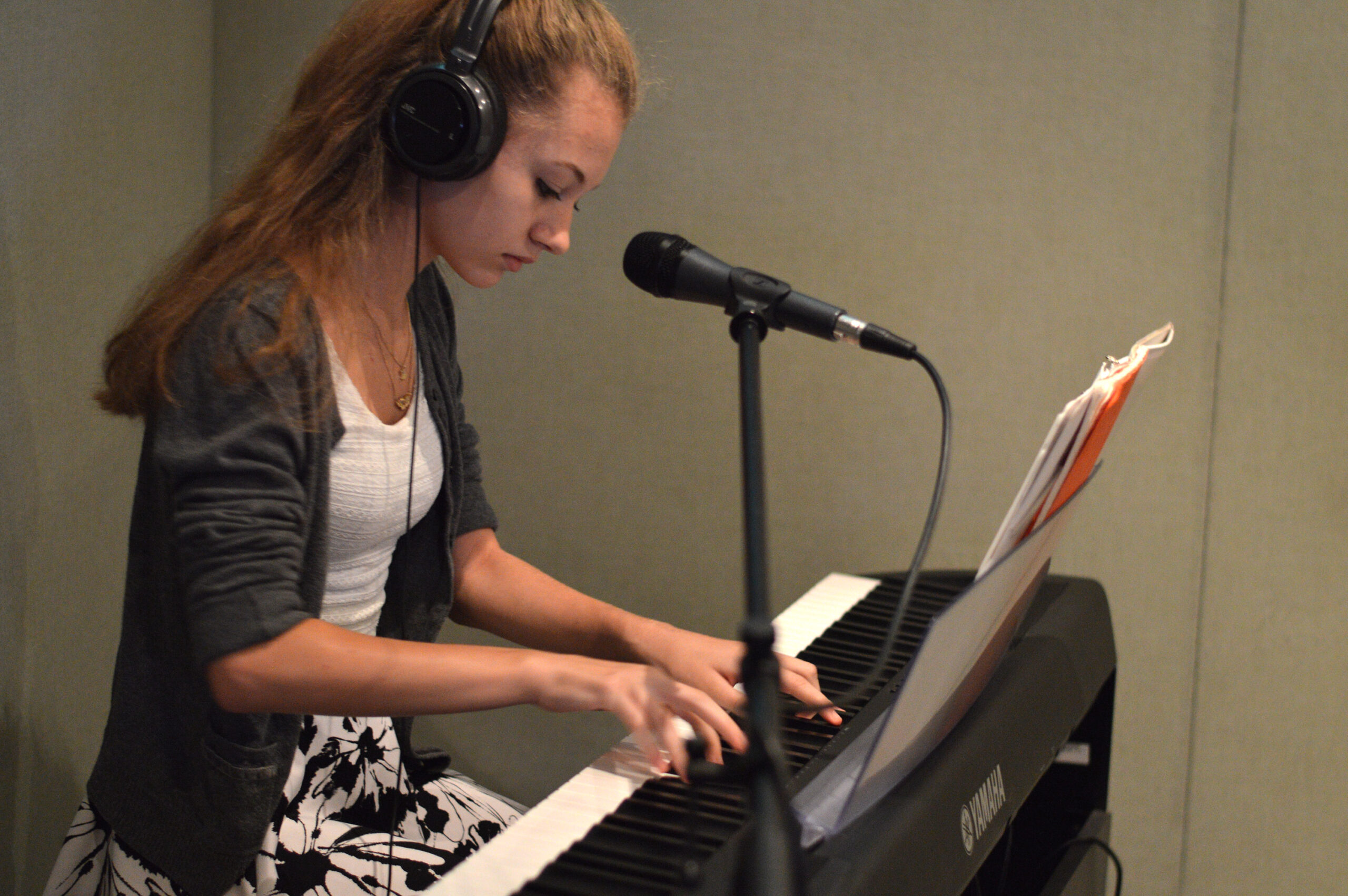 A teen wearing headphones playing a piano keyboard in a radio studio.