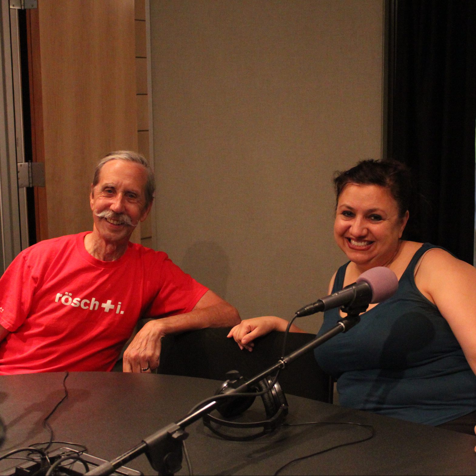 Two adults sitting behind microphones in a radio studio