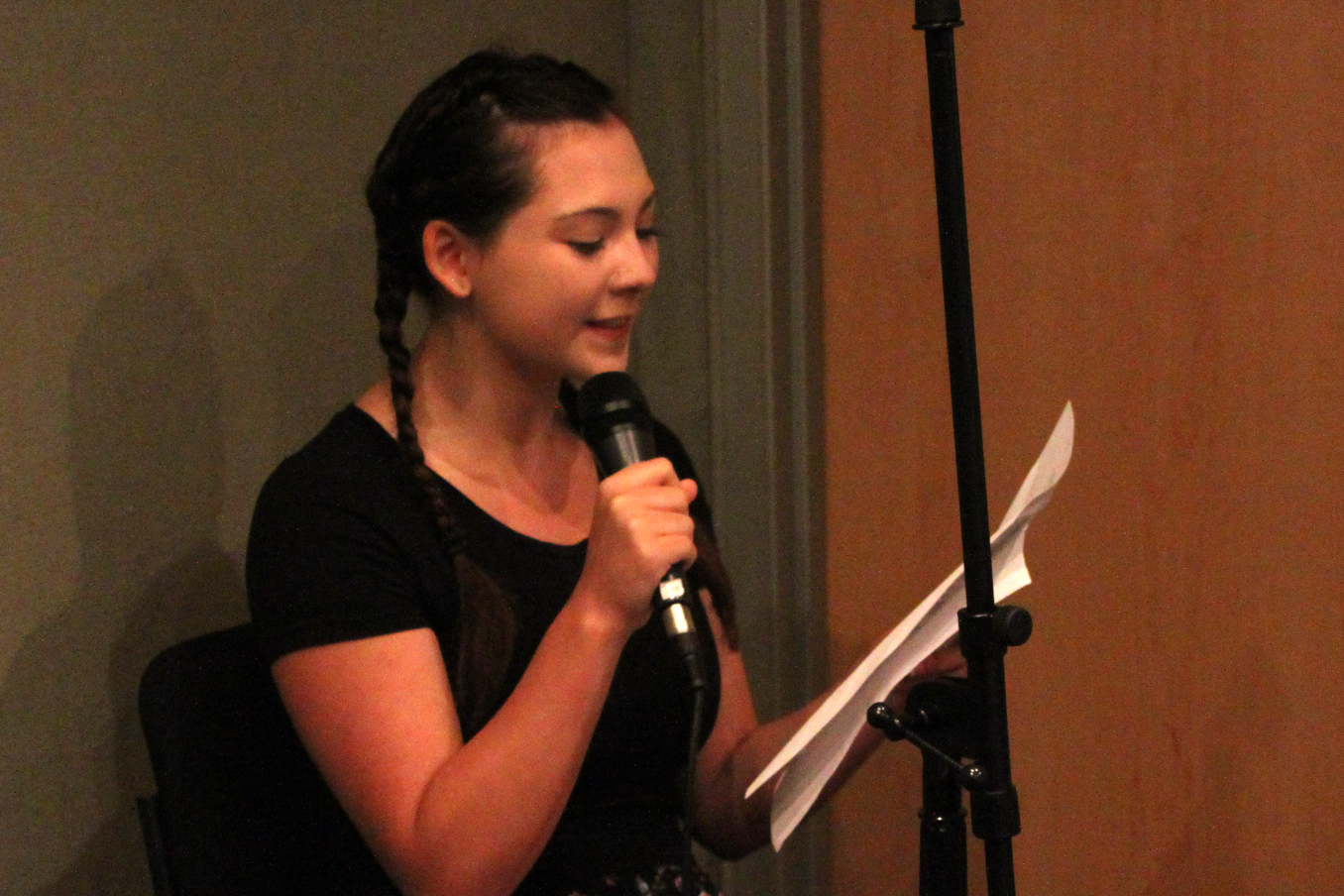 A teen singing into a microphone holding a piece of paper in a radio studio