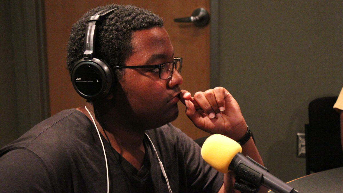 A youth wearing headphones sitting behind a microphone in a radio studio