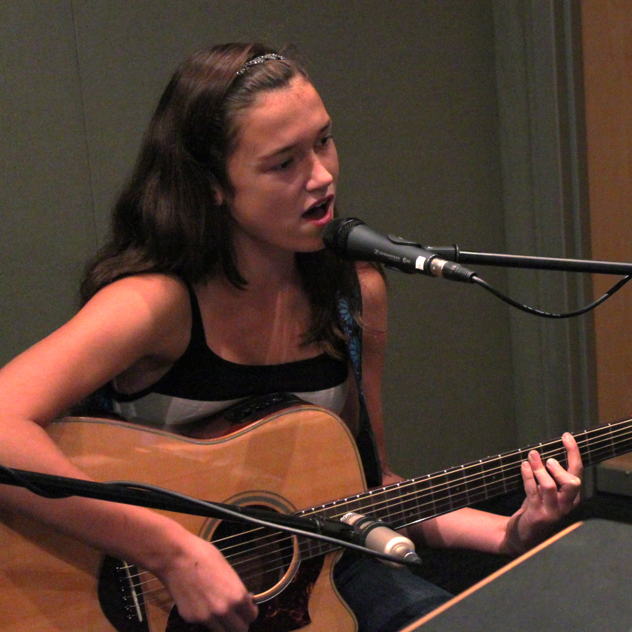 A teen playing an acoustic guitar and singing into a microphone in a radio studio