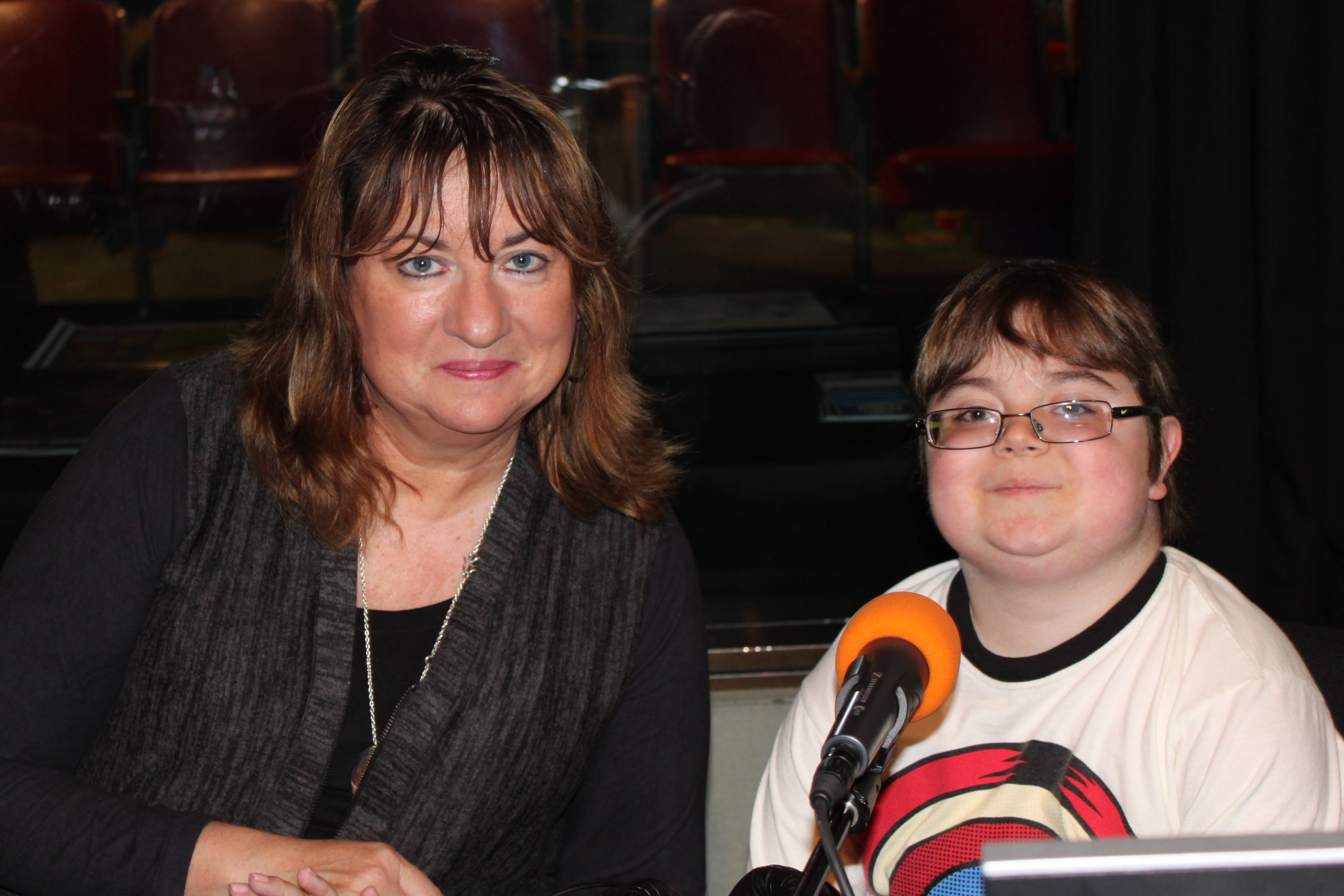 An adult and a youth sitting behind a microphone in a radio studio