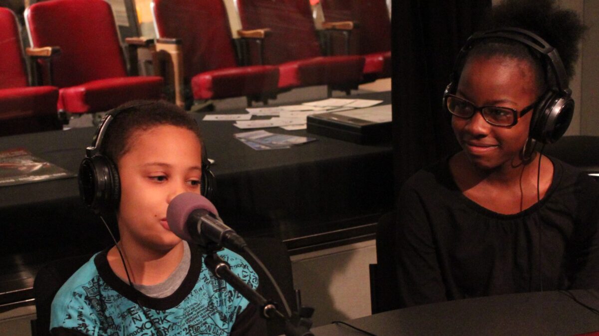 Two youth wearing headphones speaking into microphones in a radio studio