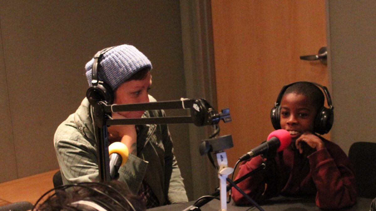 Two youth wearing headphones speaking into microphones in a radio studio