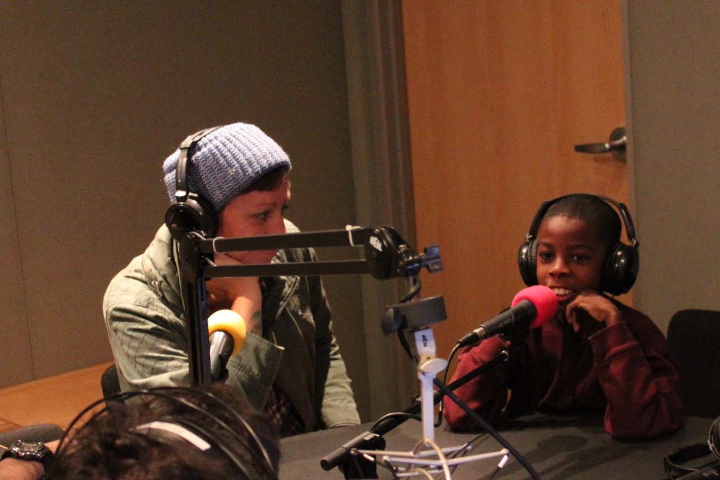 Two youth wearing headphones speaking into microphones in a radio studio
