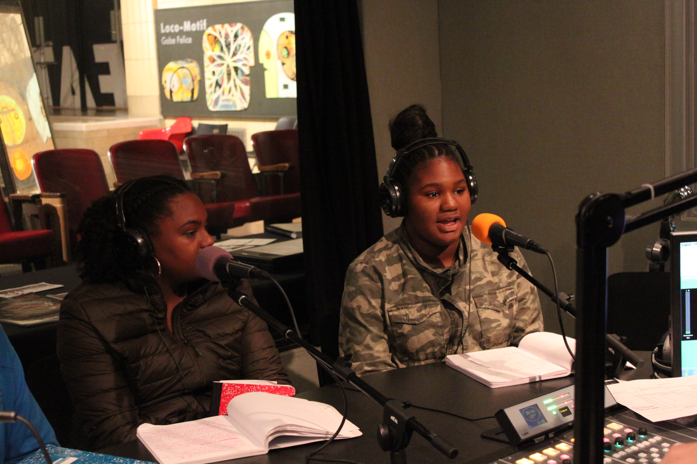 Two youth wearing headphones speaking into microphones in a radio studio