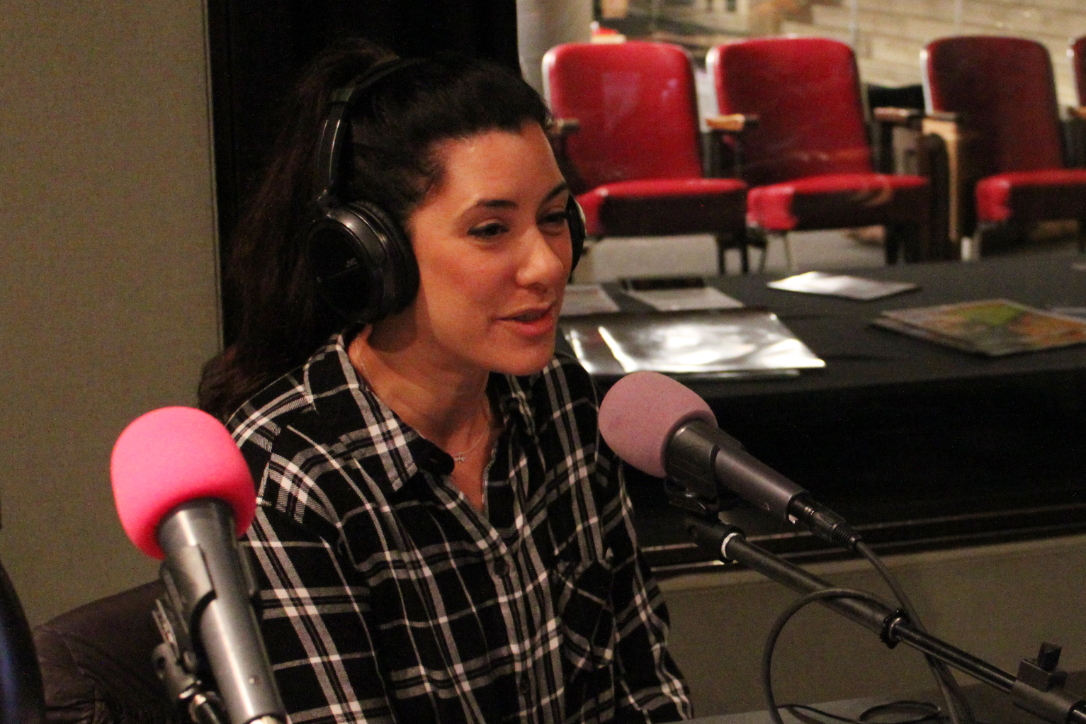 An adult wearing headphones speaking into a microphone in a radio studio