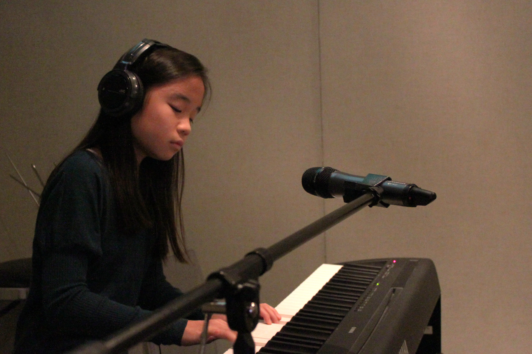 A teen wearing headphones playing a piano keyboard in a radio studio