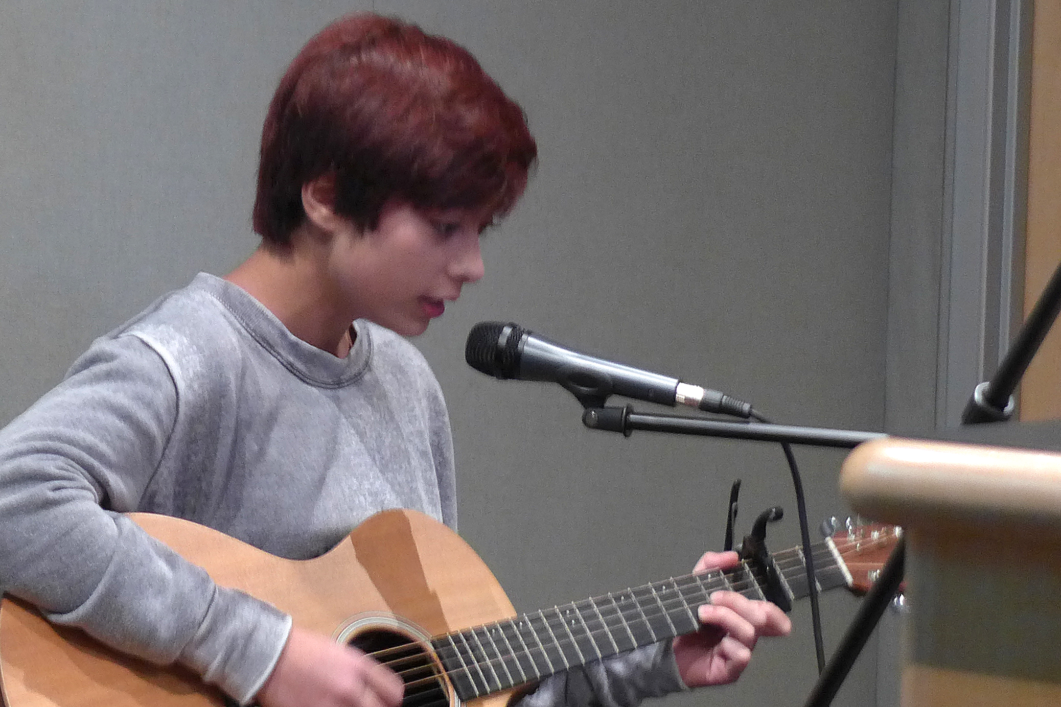 A teen playing an acoustic guitar and singing in a radio studio