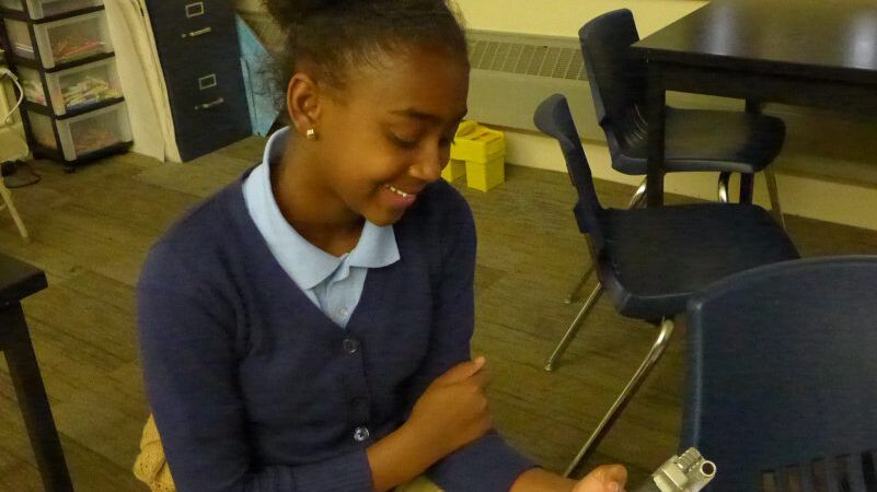 A youth holding a portable recorder smiling in a classroom