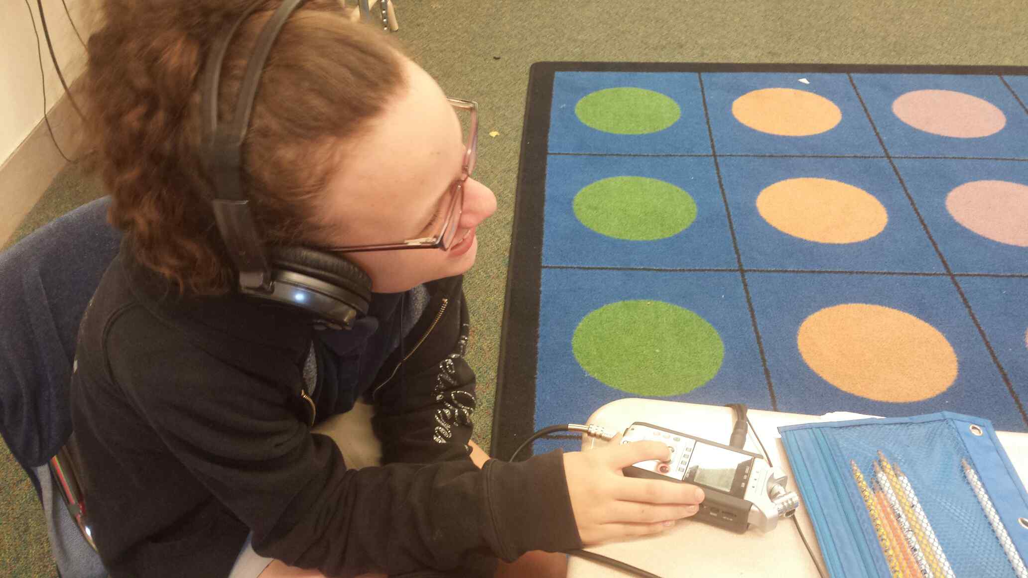 A youth wearing a pair of headphones interacting with a portable recorder in a classroom