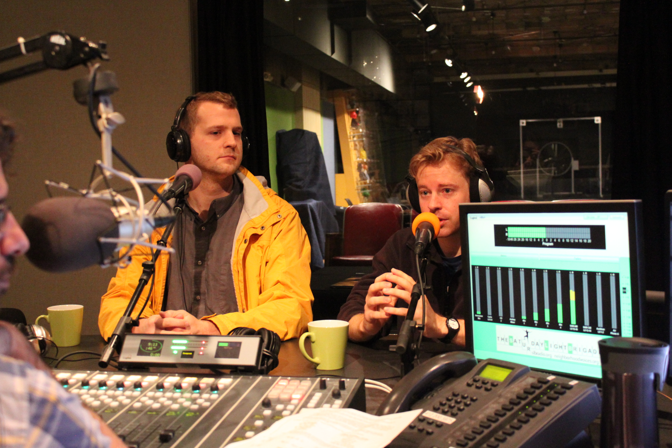 Two adults wearing headphones speaking into microphones being interviewed in a radio studio