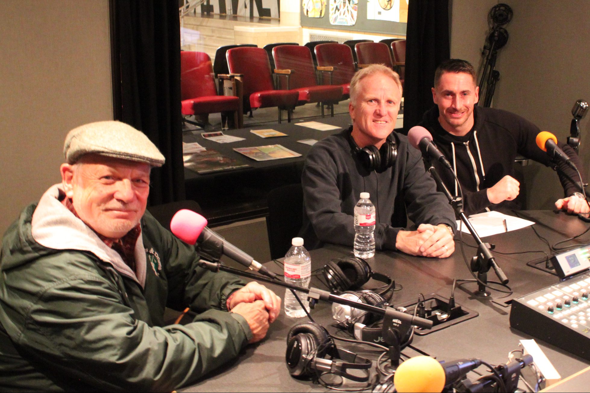Three adults smiling while sitting behind microphones in a radio studio