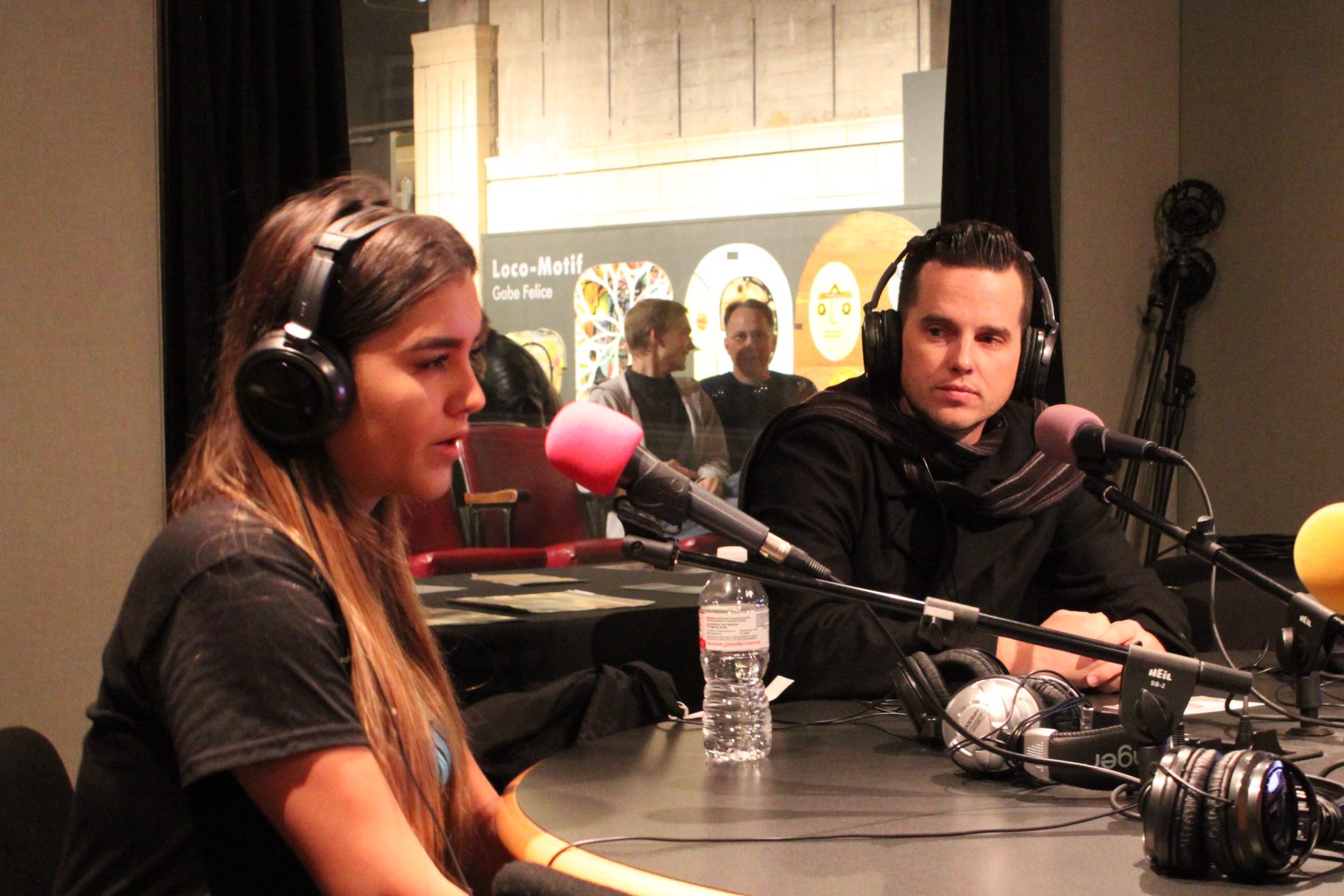 Two teens wearing headphones speaking into microphones in a radio studio
