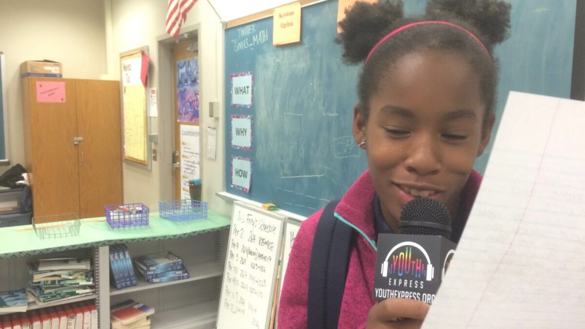 A youth holding a piece of paper speaking into a microphone in a classroom