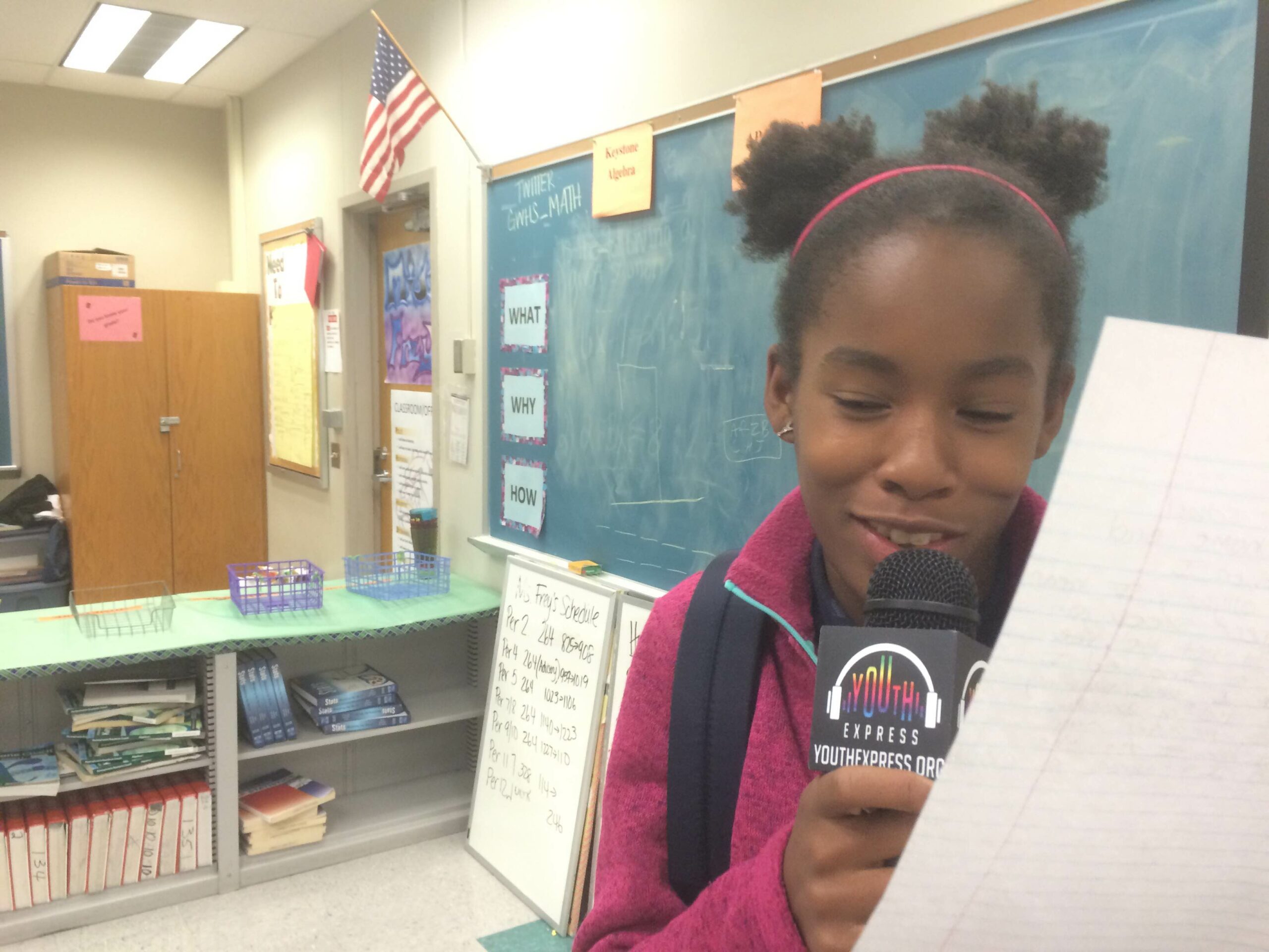 A youth holding a piece of paper speaking into a microphone in a classroom