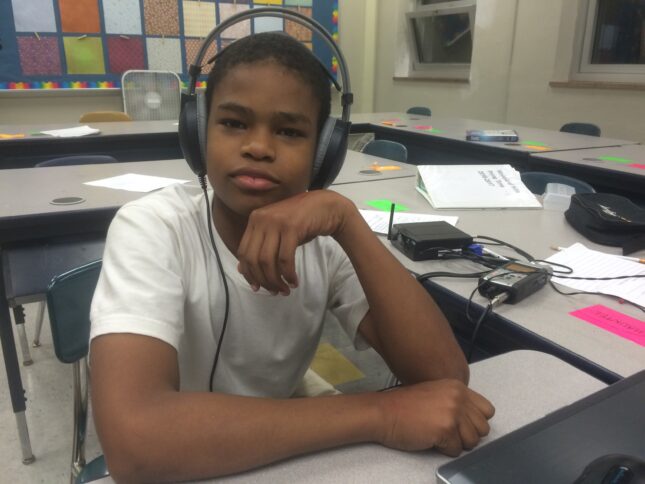 A youth wearing headphones posing while sitting at a classroom desk