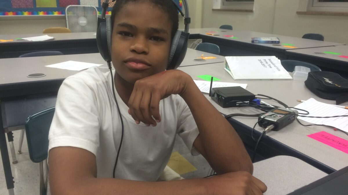 A youth wearing headphones posing while sitting at a classroom desk