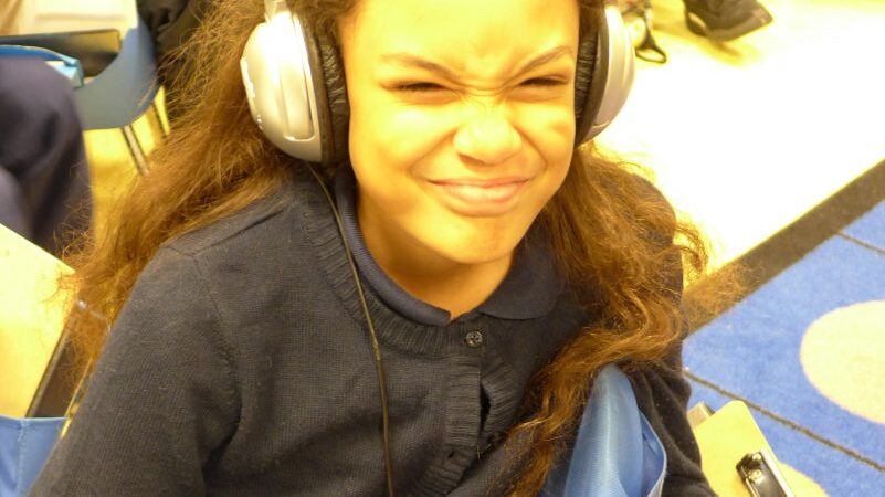 A youth wearing headphones grimacing at the camera in a classroom