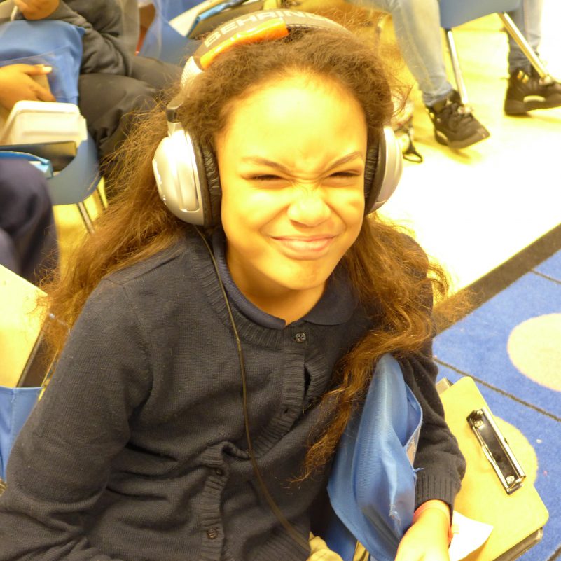 A youth wearing headphones grimacing at the camera in a classroom