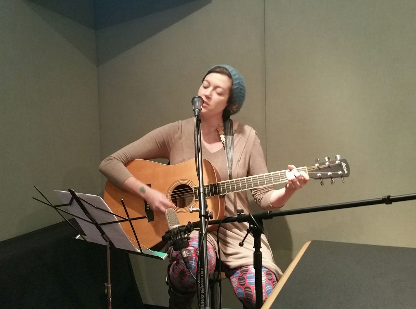An adult playing acoustic guitar and singing into a microphone in a radio studio