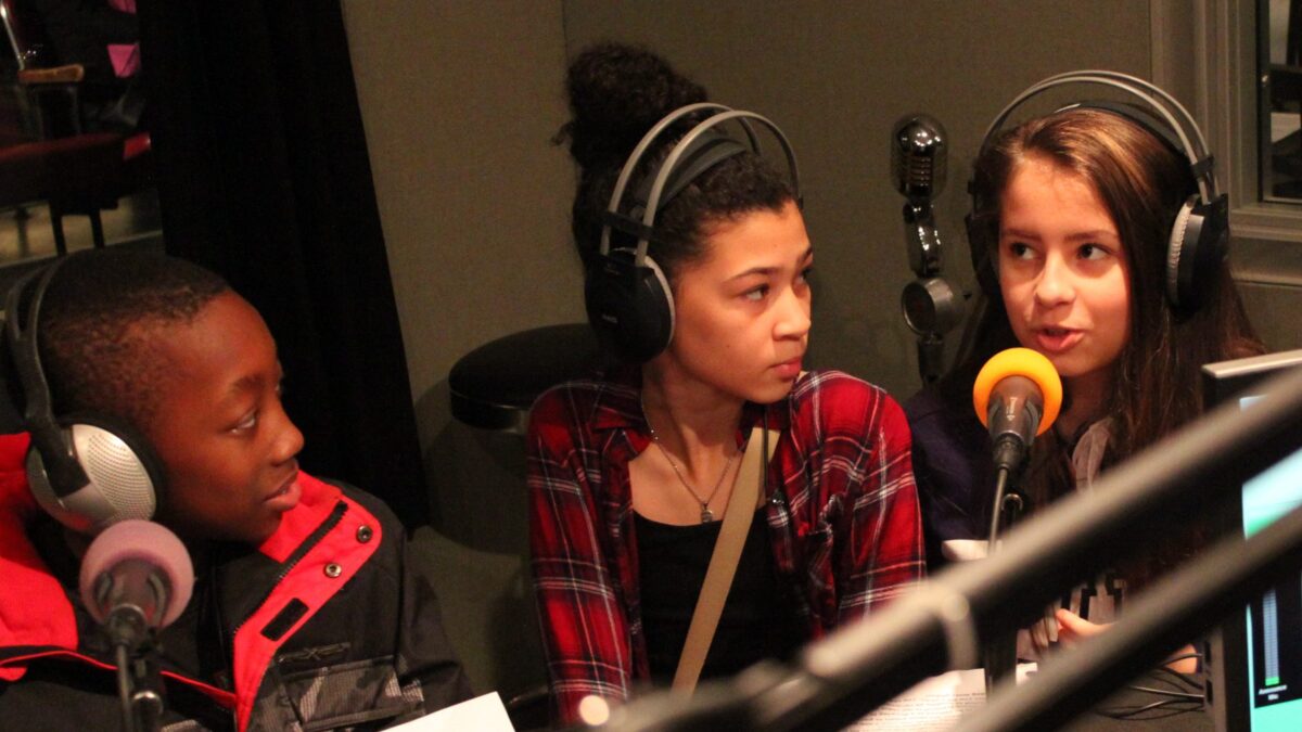 Three youth wearing headphones speaking into microphones in a radio studio