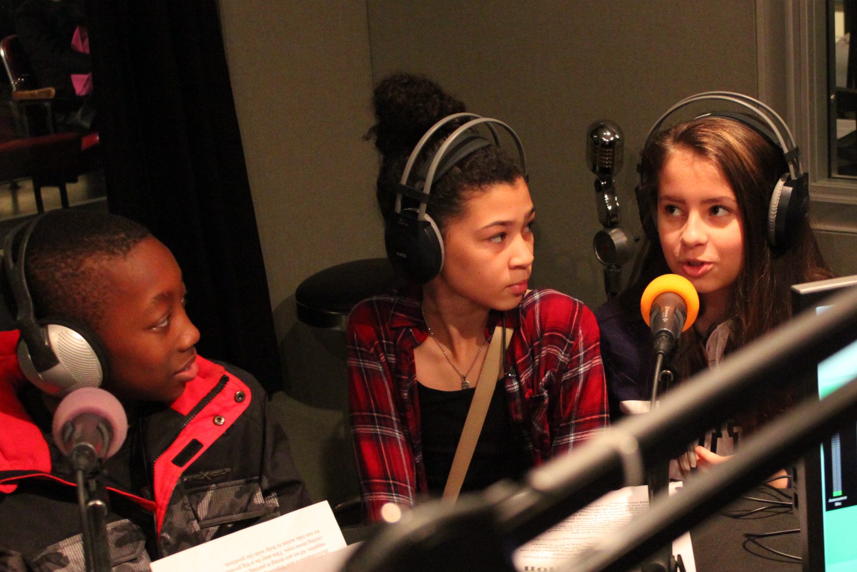 Three youth wearing headphones speaking into microphones in a radio studio