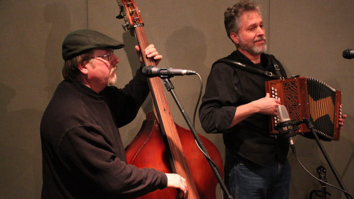An adult paying upright bass and an adult playing accordion in a radio studio
