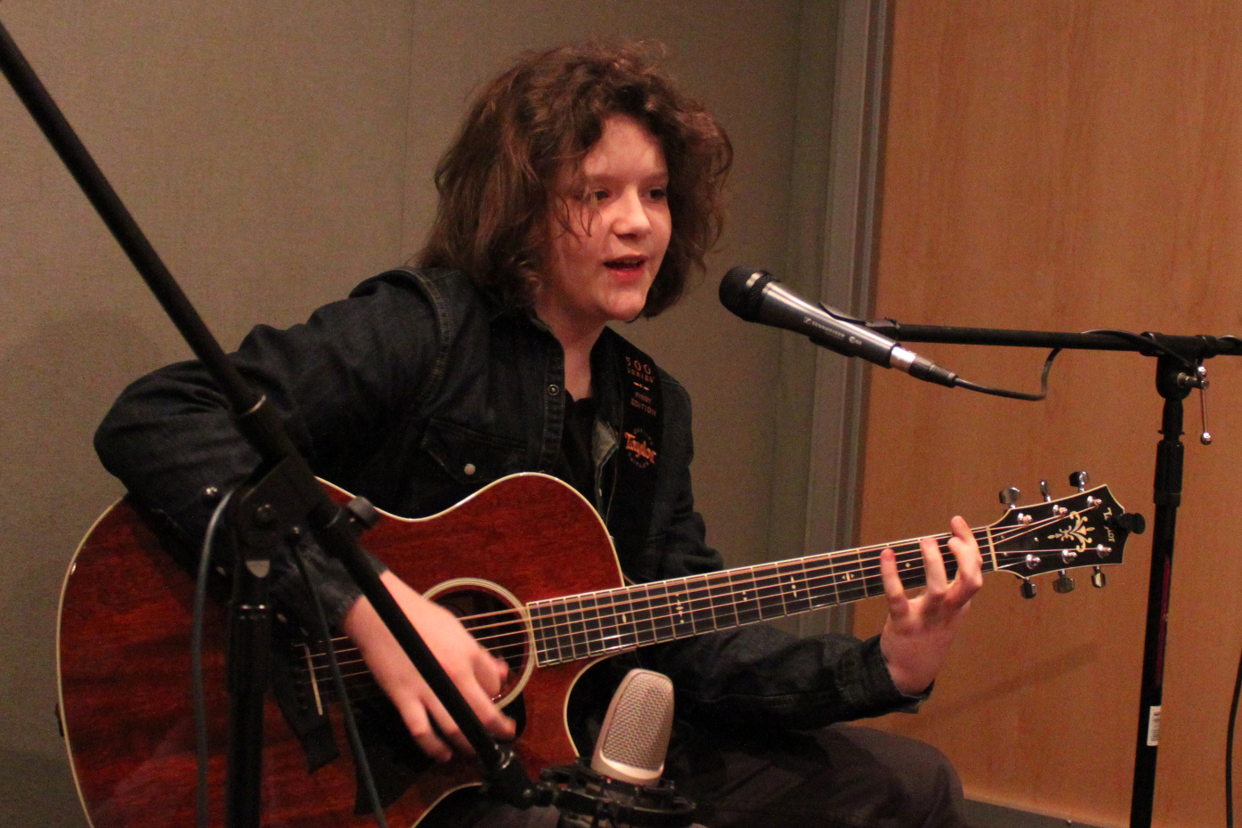 A teen playing acoustic guitar and singing into a microphone in a radio studio