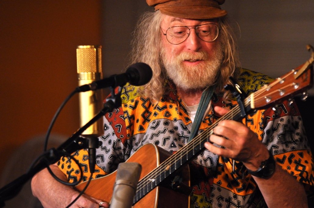 An adult playing acoustic guitar and singing into microphone
