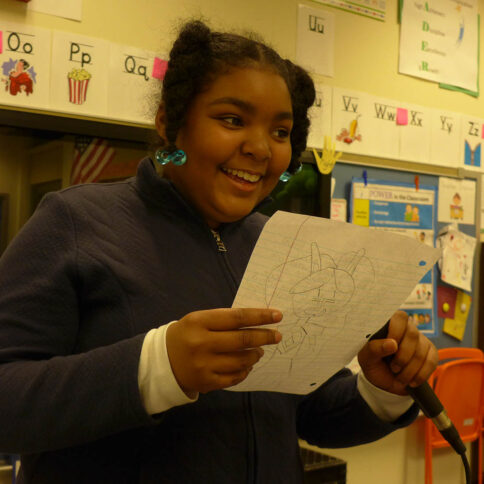 A youth holding and reading a piece of paper in a classroom