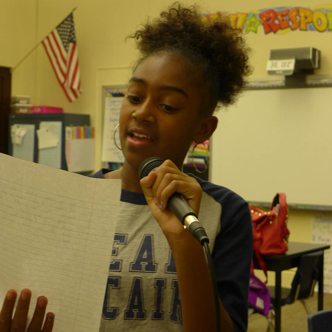 A youth holding a piece of paper reading into a microphone in a classroom