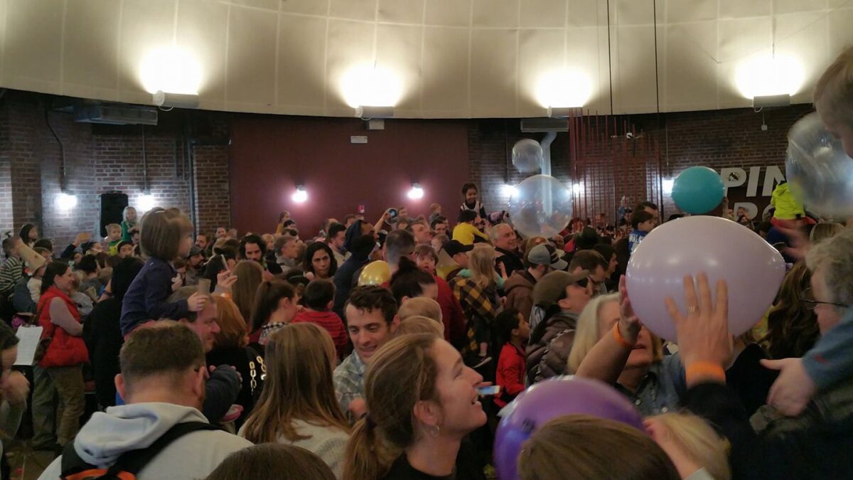 A large gathering on individuals in a large circular room tossing balloons in the air