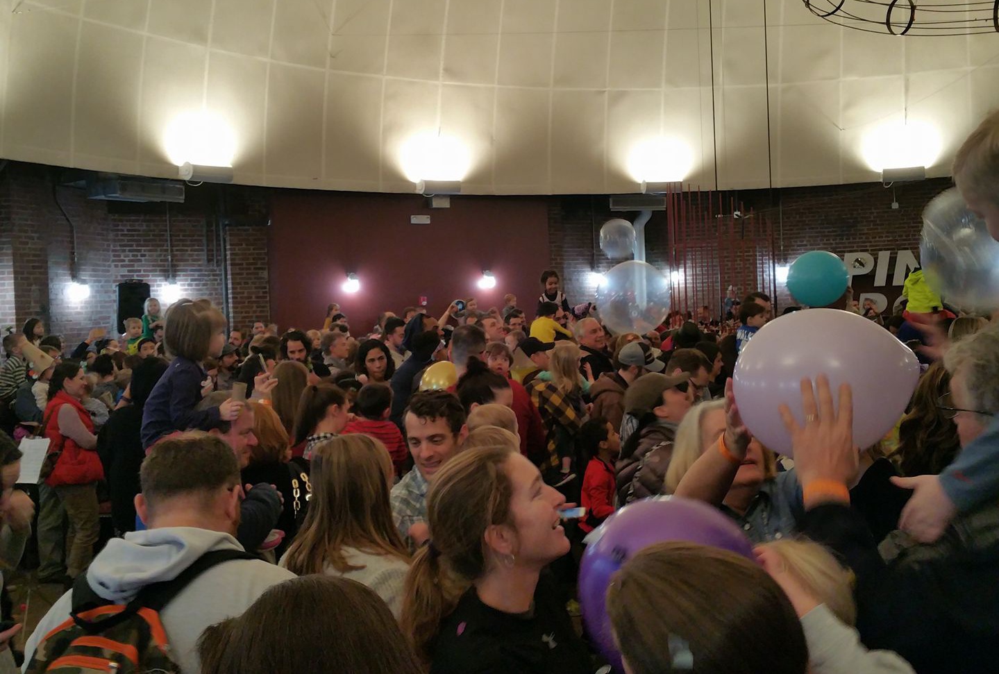 A large gathering on individuals in a large circular room tossing balloons in the air