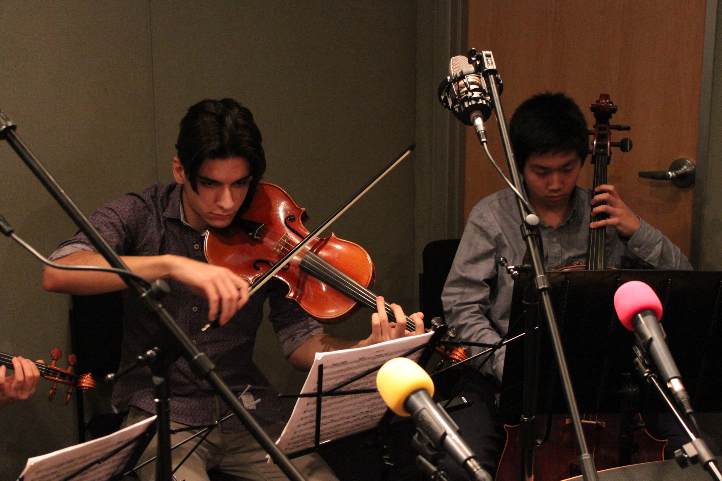 A teen playing viola and a teen playing cello looking at sheet music on music stands in a radio studio