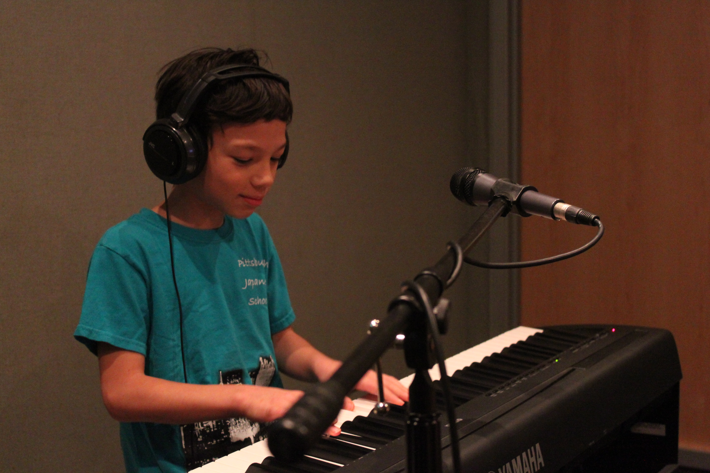 A youth wearing headphones playing a piano keyboard in a radio studio