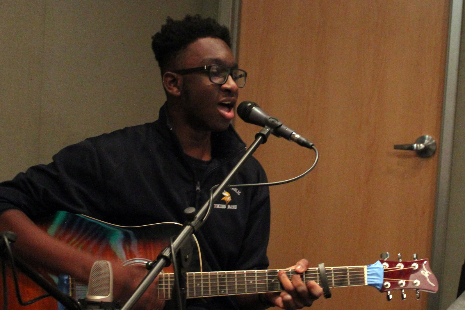 A teen playing an acoustic guitar and singing into a microphone in a radio studio