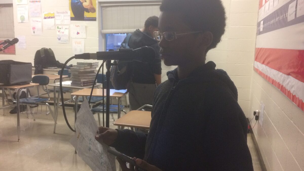 A youth reading a piece of paper into a microphone in a classroom