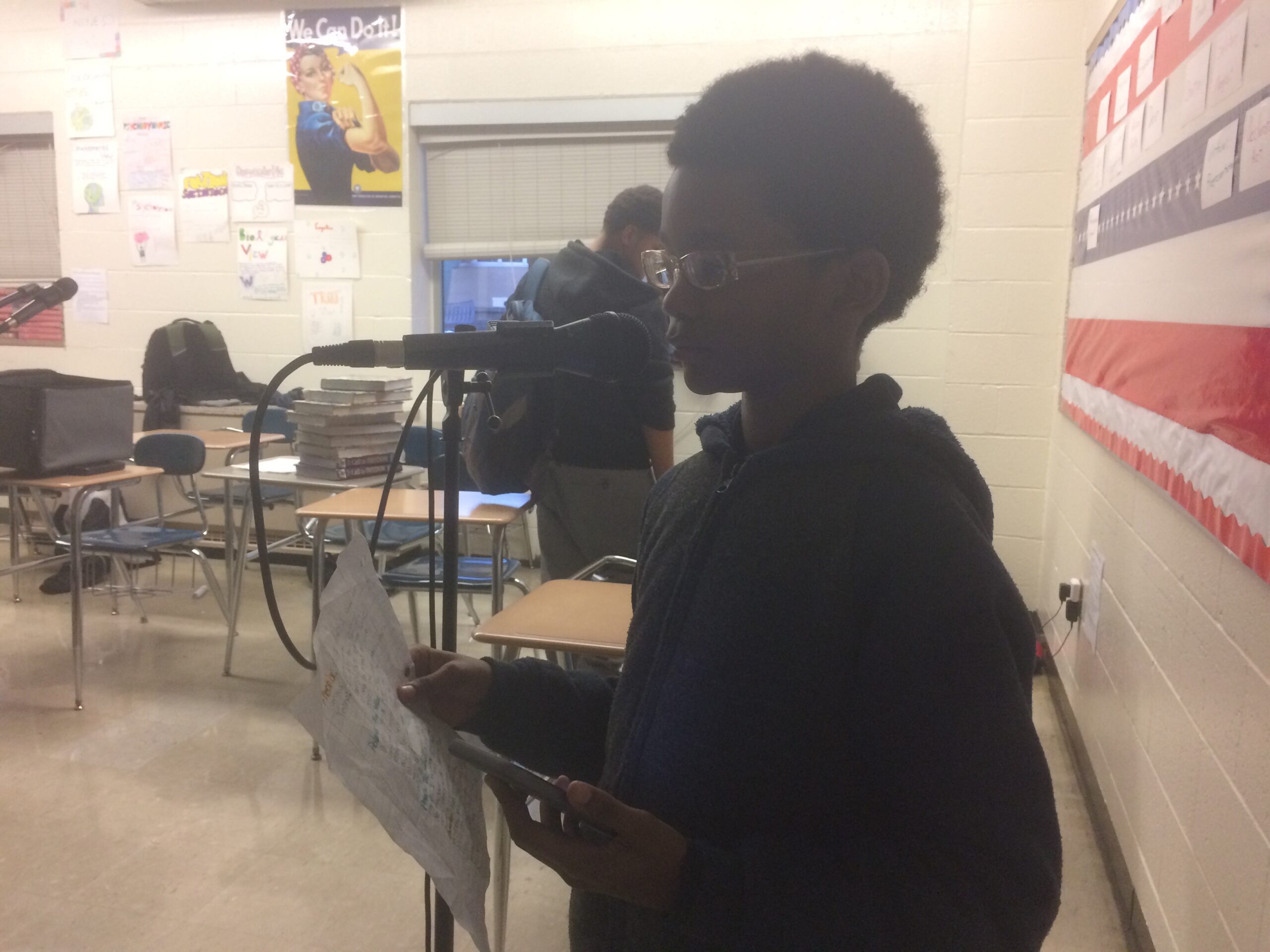 A youth reading a piece of paper into a microphone in a classroom