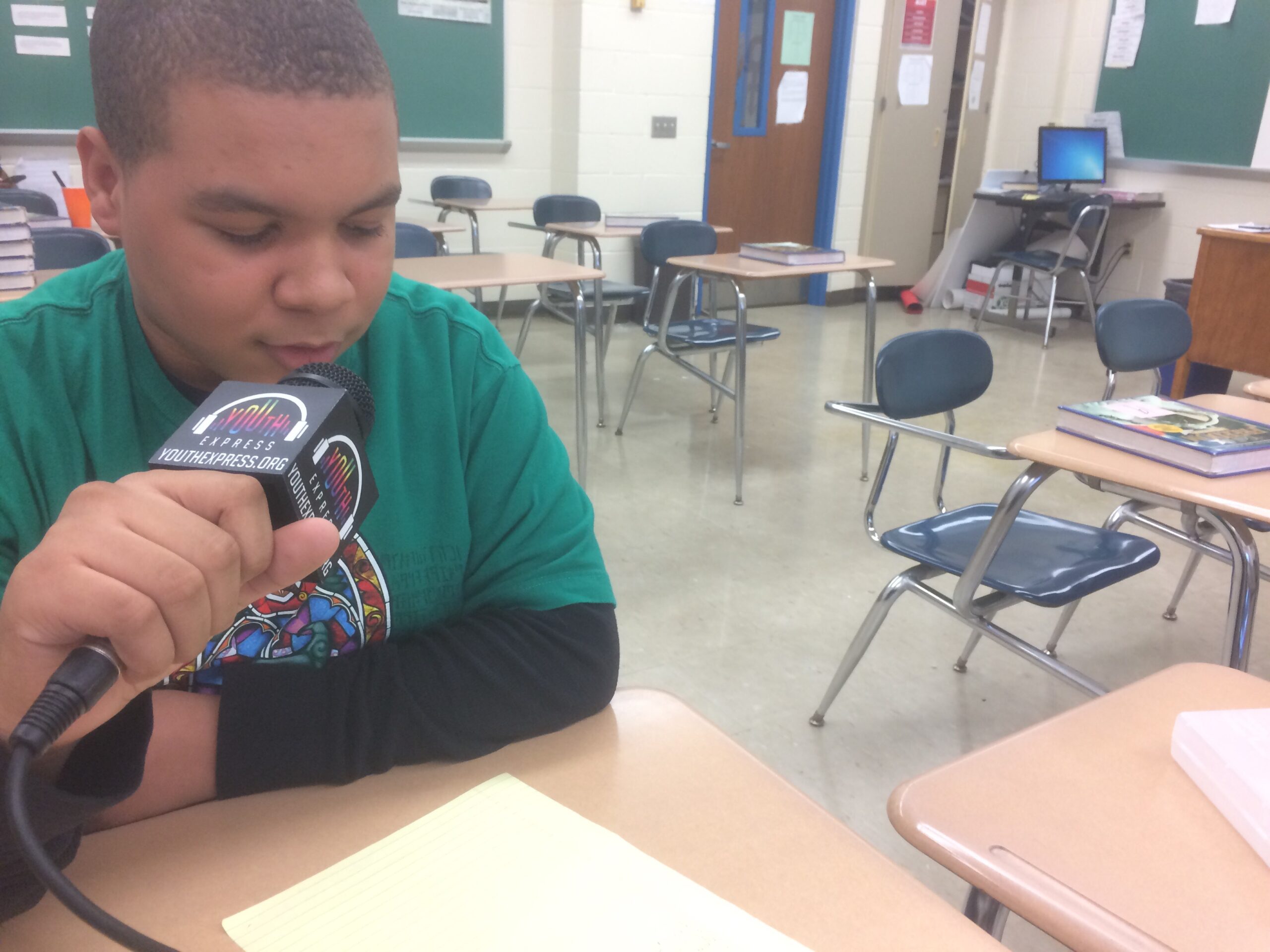 A youth holding a microphone reading a piece of paper in a classroom
