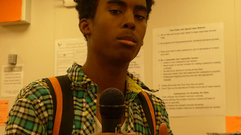 A teen holding a microphone and giving a thumbs up in a radio studio