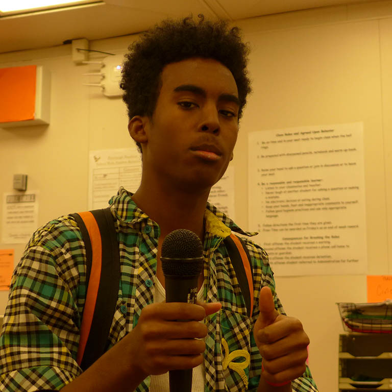 A teen holding a microphone and giving a thumbs up in a radio studio
