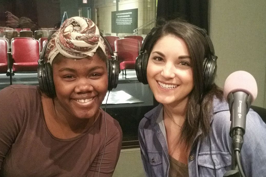 A teen and an adult wearing headphones smiling behind microphones in a radio studio.