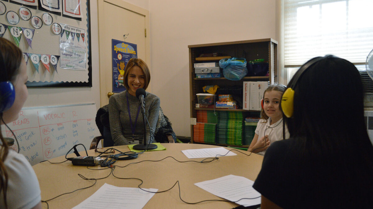 Three youth wearing headphones interviewing an adult speaking into a microphone in a library