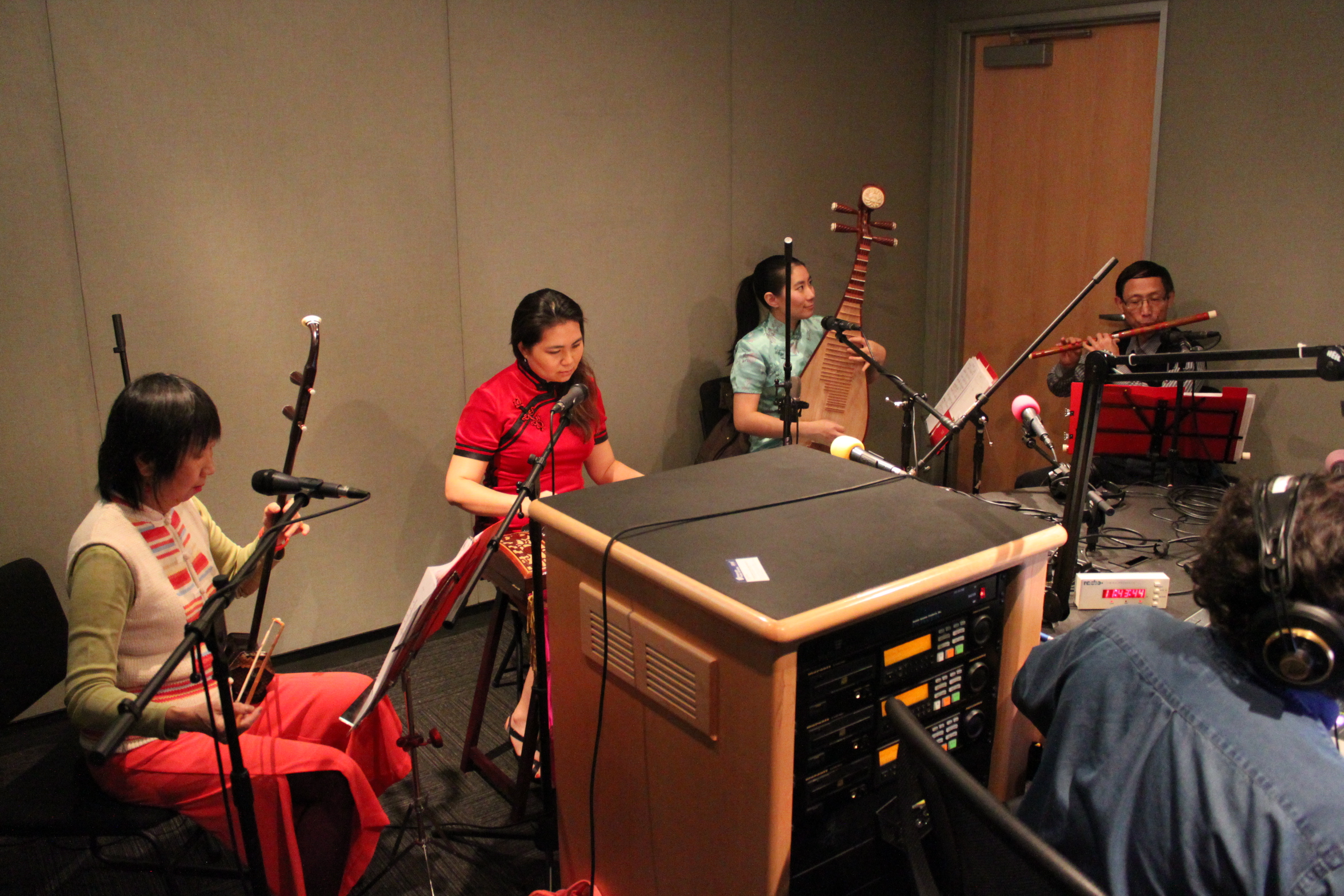 Four adults playing traditional Chinese instruments looking at sheet music on music stands in a radio studio