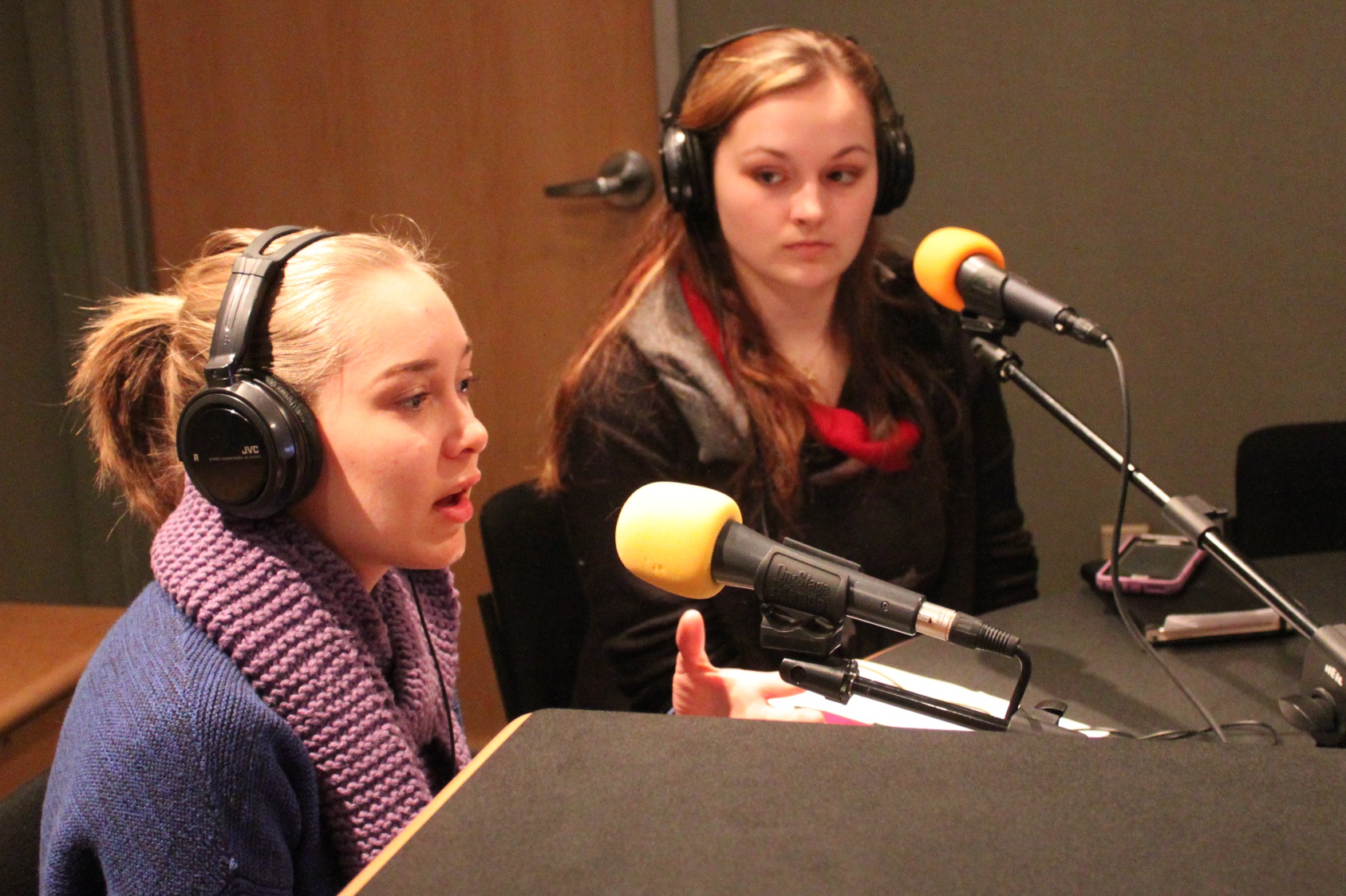 Two teens wearing headphones speaking into microphones in a radio studio