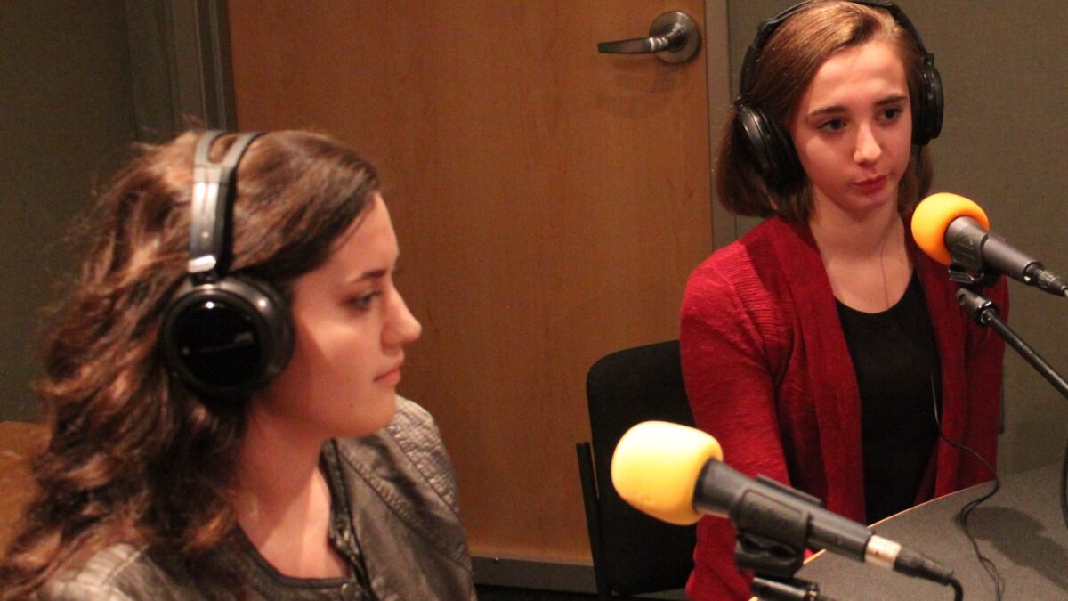 Two teens wearing headphones speaking into microphones in a radio studio